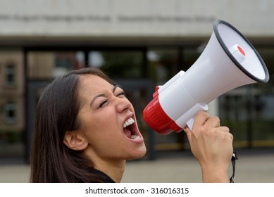 Angry young woman yelling over a megaphone or bullhorn as she participates in a street demonstration or protest airing her grievances, close up side view of her face - Powered by Shutterstock