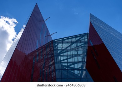 Angular Architectural Design of a Museum: A dynamic view of a museum’s sharp, angular red and glass facade under a clear sky.