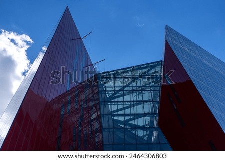 Angular Architectural Design of a Museum: A dynamic view of a museum’s sharp, angular red and glass facade under a clear sky.