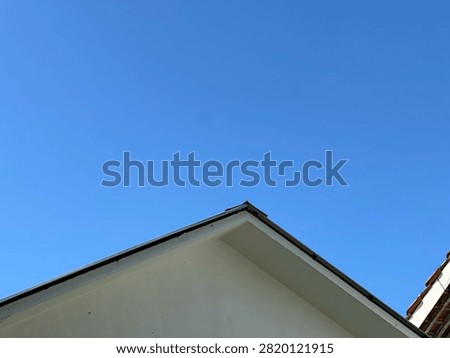 The angular gable roof of a white building stands sharply against a vast, clear blue sky