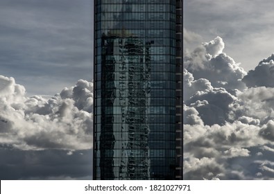 Angular geometric mirror cladding on a modern building with repeating structure and reflected sky and clouds. No focus, specifically.