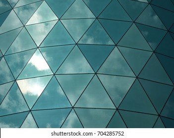 angular geometric mirror cladding on a modern building with repeating structure and  reflected sky and clouds