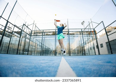 Angular photo of a girl in sportswear jumping to hit a ball during an outdoor paddle match. Concept of women playing paddle, paddle for girls. Paddle sport.