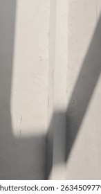 Angular shadows from harsh sunlight fall on a textured white wall, creating an abstract minimalist geometric pattern. Architectural detail.