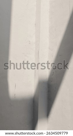 Angular shadows from harsh sunlight fall on a textured white wall, creating an abstract minimalist geometric pattern. Architectural detail.