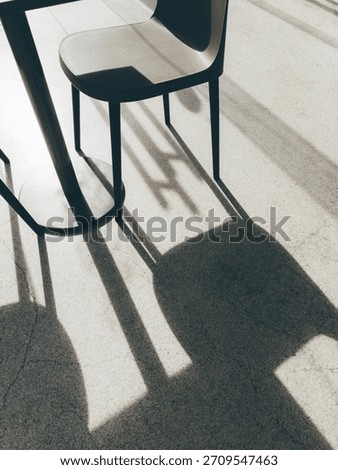 Angular shadows of metal chairs fall across a smooth grey floor, creating a dramatic contrast of shapes and lines in natural light.