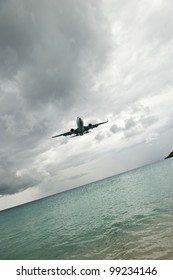 An angular shot of an airplane flying over the ocean, in cloudy weather; it looks like it's about to rain.