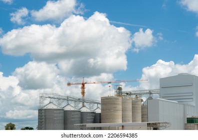 Animal Feed Factory Construction Site. Agricultural Silo At Feed Mill Factory. Tank For Store Grain And Construction Crane. Seed Stock Tower For Commercial Animal Feed Production. Animal Food Industry