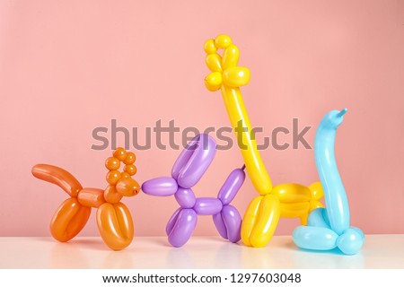 Animal figures made of modelling balloons on table against color background