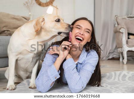 Animal Love Concept. Closeup of labrador retriever licking woman's cheek, lying on the floor in living room