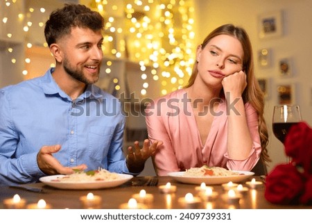 Animated man speaking and gesturing with his hands across the dinner table to a woman who appears uninterested or lost in thought, with romantic lighting