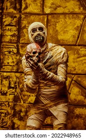 An Animated Mummy Of A Man Holds A Human Skull In His Hands. Halloween. Ancient Egyptian Mythology.