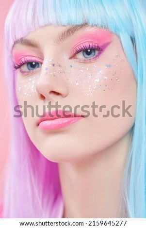 Anime makeup. Pretty girl with bright makeup, glitter freckles and in colored violet-blue wig on a pink background. Hairstyle, hair coloring, make-up. Japanese anime style. 