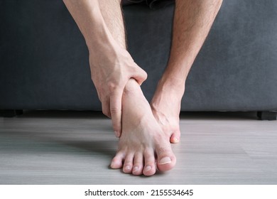 Ankle Pain man sitting on wooden background holding her feet. Health concept.