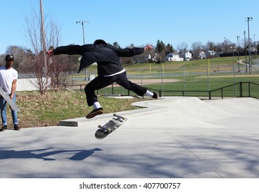 ANN ARBOR, MI/USA: APRIL 5, 2016 Young Man In Black Jacket Attempts Stunt At Veterans Memorial Park Skateboard Park As Another Young Man Watches. 