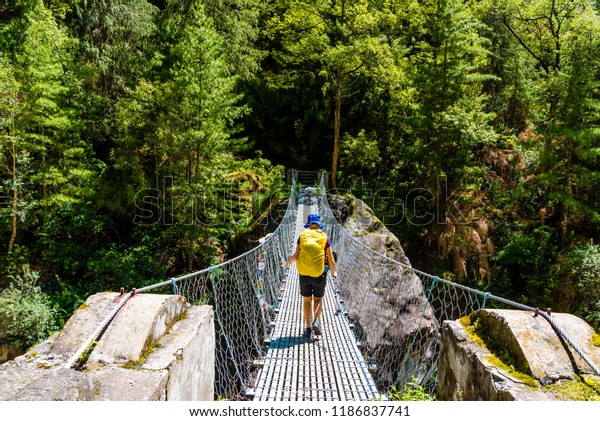Annapurna Conservation Area, Nepal - July 19, 2018\
: Woman backpacker on trekking path crossing a suspended bridge in\
Annapurna Conservation Area, a hotspot destination for mountaineers\
in Nepal