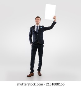 Announcement Concept. Confident Business Man Holding White Advertisement Board In Hand, Standing Isolated On White Studio Background, Raising Lifting Sign Board Up, Full Body Length, Vertical Banner