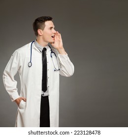 Announcement Message. Profile Portrait Of A Shouting Doctor. Waist Up Studio Shot On Gray Background.