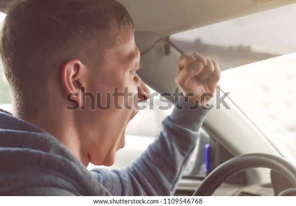 Annoyed and angry driver screaming and shouting\
on the other driver and threatens with fist. Bad and aggressive\
behavior on road\
concept.