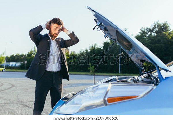 an
annoyed and angry man, near a broken car, tries to call an
insurance agent and a repair crew. for car
repair