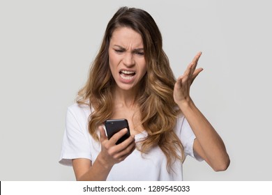 Annoyed Angry Young Woman Mad About Spam Message Stuck Phone Looking At Smartphone Isolated On Blank Studio Background, Furious Teen Girl Having Problem With Cellphone Irritated By Broken Mobile