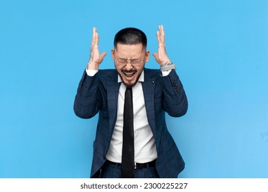 annoyed asian businessman in suit and glasses screaming in stress on blue isolated background, korean entrepreneur in business clothes is panicking and freaking out - Powered by Shutterstock