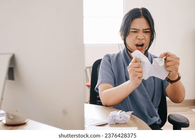 Annoyed Asian businesswoman crumples paper sheets in angry mood at table in office. - Powered by Shutterstock