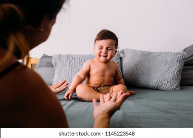 Annoyed Baby Crying Sitting On The Bed In The Room Wearing Shorts, Mom Is In The Frame Of The Image Animating Him, Frustration Concept