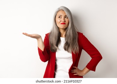 Annoyed And Confused Asian Business Woman Spread Hand Sideways And Shrugging, Looking Questioned Left, White Background