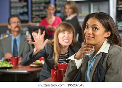 Annoyed Coworker Behind Smiling Business Woman In Cafeteria