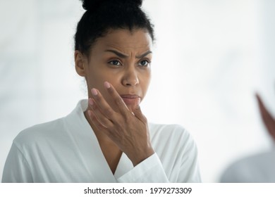 Annoyed frustrated young Afro American woman feeling dryness, after morning shower, looking in mirror, scanning facial skin with frowning face. Skincare problems, dry skin concept - Powered by Shutterstock