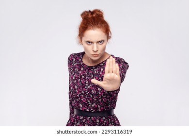 Annoyed ginger woman wearing dress making stop gesture with her palm outward, saying no, expressing denial or restriction, negative human emotions. Indoor studio shot isolated on gray background. - Shutterstock ID 2293116319