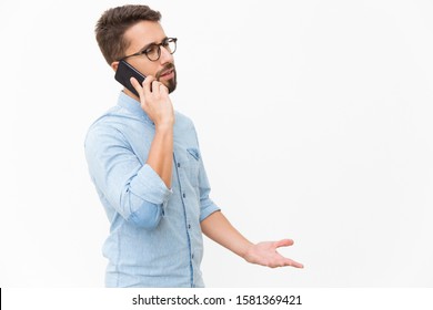 Annoyed guy speaking on mobile phone, arguing with talk partner. Handsome young man in casual shirt and glasses standing isolated over white background. Phone talk concept - Powered by Shutterstock