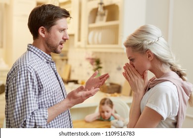 Annoyed Husband Trying To Explain Something To His Wife With Their Little Daughter On Background