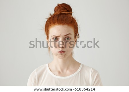 Annoyed irritated young red-haired female with freckles blowing her cheeks, frowning, feeling frustrated with something. Human facial expressions, emotions and feelings. Fatigue or boredom concept
