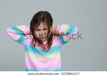 Annoyed little girl covering her ears from loud sound on grey background. Space for text