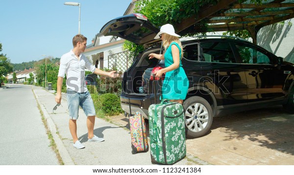 Annoyed man argues with his wife where all the\
luggage will go in their car parked in front of their house.\
Husband gets frustrated with excited wife over overpacking for\
their short summer\
vacation.