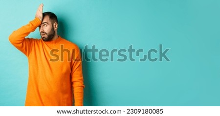Annoyed man roll eyes and making facepalm, standing over turquoise background.