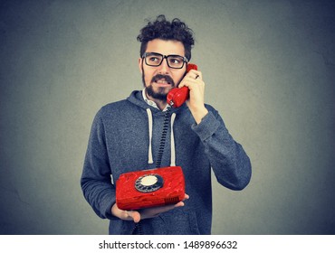 Annoyed Man Talking On An Old Fashioned Telephone, Displeased With Long Waiting Time For Customer Service 