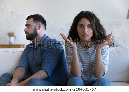 Annoyed married couple sitting on couch apart, after conflict, arguing, row. Serious angry wife looking at camera, tired husband turning away. Marriage crisis, counseling, relationships concept