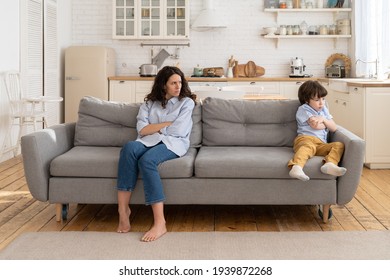 Annoyed Mom And Stubborn Child Sitting On Couch At Home, Ignoring Each Other, Posture Of Discontent. Sad Mother Disobedient Kid Son Sitting Apart On Sofa With Arms Crossed, Not Talking After Quarrel.