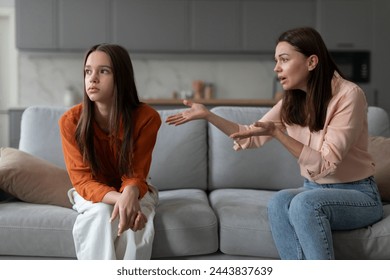 Annoyed mother gesturing to teen daughter sitting on couch, sad teen girl looking away, relationship problems with teenagers and generation gap concept - Powered by Shutterstock