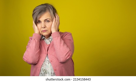 Annoyed And Scared Old Grandma Holding On To Her Head Due To Loud Noises. Elderly Lady Having A Migrane.