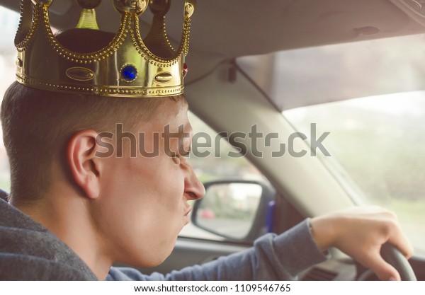 Annoyed selfish driver with golden crown above\
his head driving a car. Disdainful and boorish attitude on the road\
concept.