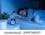 Annoyed, stressed, anxiety asian young woman suffering from insomnia with alarm clock time, frustrated awake on bed at night, health care problem, disturbed trouble of loud noise, unable sleepless.