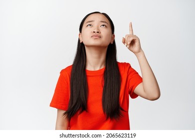 Annoyed Teen Asian Girl Pointing And Looking Up With Tired, Fed Up Face Expression, Being Pissed Off, Standing In Red T-shirt Over White Background