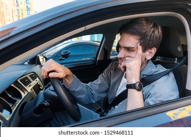 Annoyed Tired Young Man Is Riding Driving Car. Businessman Is Late For Meeting. Driver Brunette In Grey Suit Stuck In Traffic Jam. Stressful Situations On Roads And Fast Rhythm In Modern City.