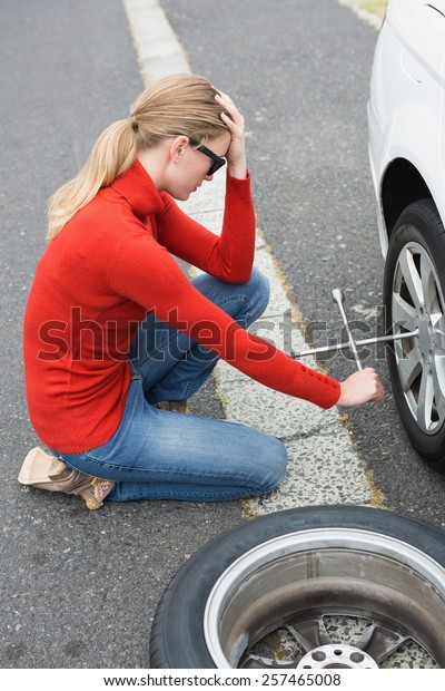 Annoyed woman\
trying to replace tire of her\
car