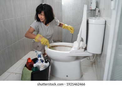 an annoyed woman wearing gloves brushing the dirty toilets in the bathroom