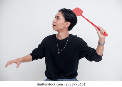 An annoyed young asian man trying to hit a fly with a flyswatter. Following and aiming at a flying bug. Isolated on a white background. - Powered by Shutterstock